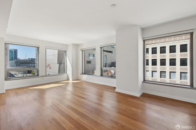 empty room with baseboards, wood finished floors, and a view of city