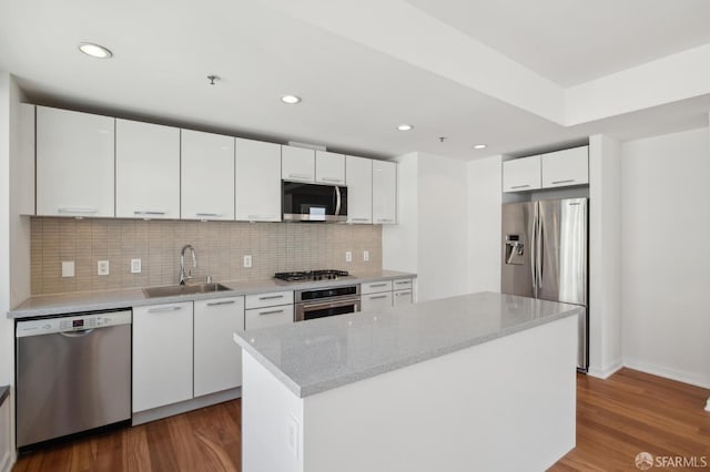 kitchen with dark wood-type flooring, a sink, backsplash, appliances with stainless steel finishes, and white cabinets