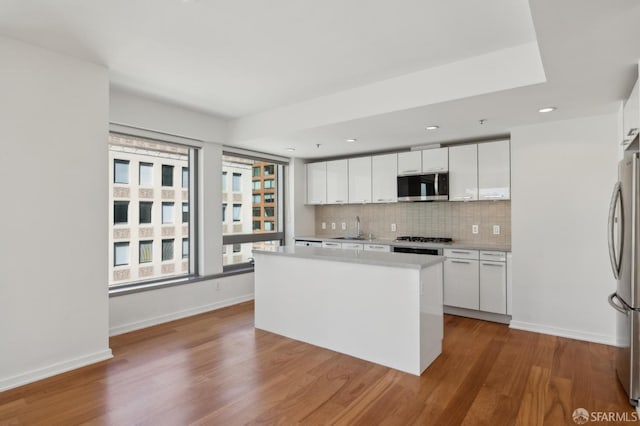 kitchen featuring backsplash, white cabinets, stainless steel appliances, and wood finished floors