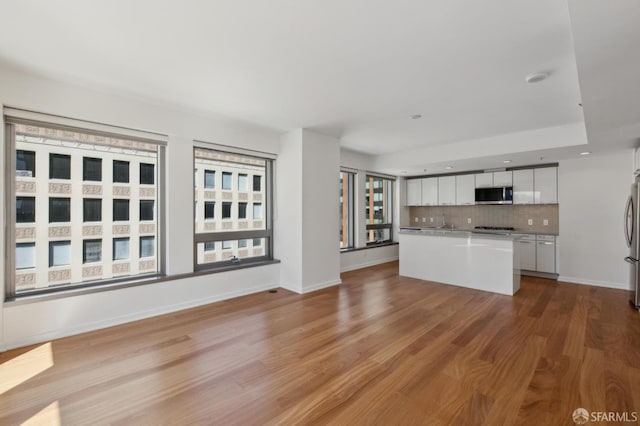 kitchen with wood finished floors, appliances with stainless steel finishes, white cabinets, decorative backsplash, and baseboards