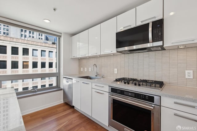 kitchen with a sink, stainless steel appliances, light countertops, white cabinets, and light wood-style floors