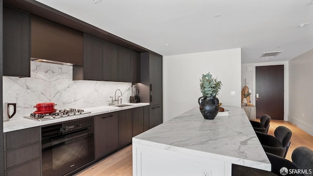 kitchen with oven, sink, stainless steel gas cooktop, light wood-type flooring, and a kitchen breakfast bar