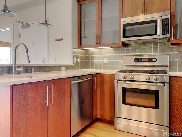 kitchen featuring pendant lighting, stainless steel appliances, tasteful backsplash, light hardwood / wood-style floors, and sink