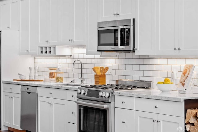 kitchen featuring appliances with stainless steel finishes, sink, tasteful backsplash, white cabinetry, and light stone countertops