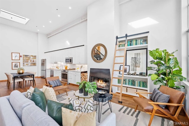 living room with light hardwood / wood-style flooring, a skylight, and a towering ceiling