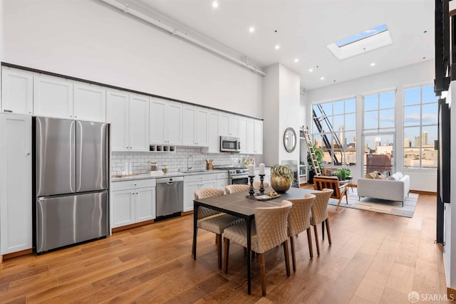 kitchen featuring white cabinets, a skylight, stainless steel appliances, light hardwood / wood-style floors, and sink