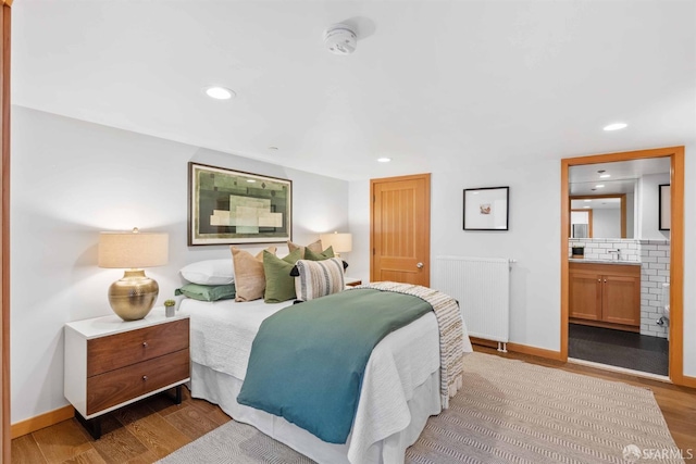 bedroom with sink, light hardwood / wood-style flooring, connected bathroom, and radiator