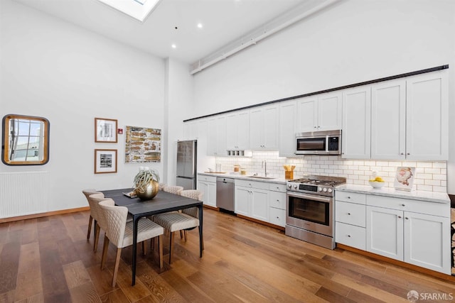 kitchen featuring sink, white cabinets, a towering ceiling, and stainless steel appliances