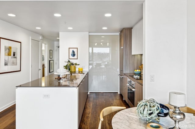 kitchen featuring stainless steel oven, dark wood-style flooring, a peninsula, black electric cooktop, and a sink