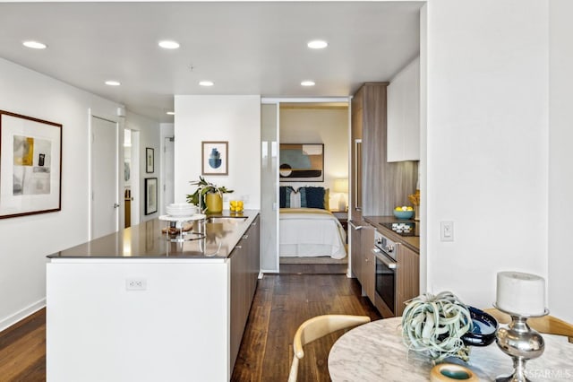 kitchen with black electric stovetop, stainless steel oven, dark wood-style flooring, a peninsula, and a sink