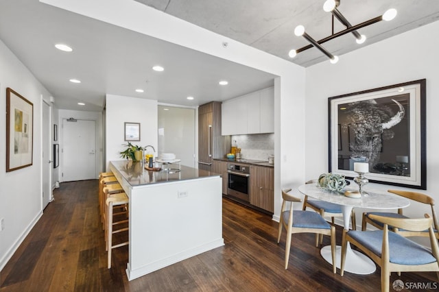 kitchen with stainless steel oven, dark wood-style floors, modern cabinets, and a breakfast bar