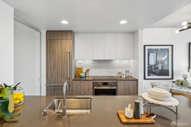 kitchen with tasteful backsplash, stainless steel oven, white cabinetry, modern cabinets, and a sink