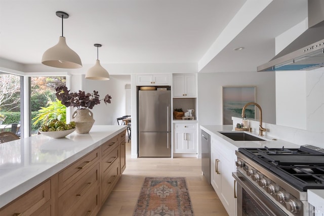 kitchen with pendant lighting, white cabinets, wall chimney exhaust hood, stainless steel appliances, and sink