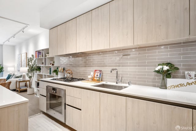 kitchen featuring decorative backsplash, light brown cabinetry, appliances with stainless steel finishes, a sink, and modern cabinets