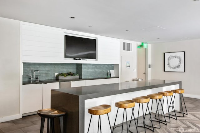 bar featuring tasteful backsplash, a sink, visible vents, and baseboards