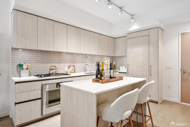 kitchen with light wood finished floors, tasteful backsplash, appliances with stainless steel finishes, a sink, and a kitchen bar