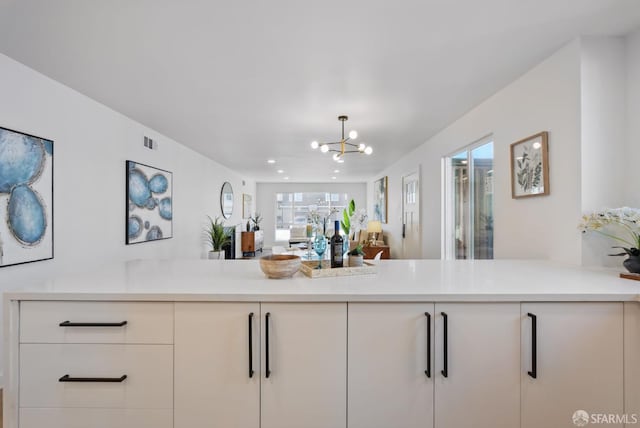 kitchen with kitchen peninsula, an inviting chandelier, and white cabinetry