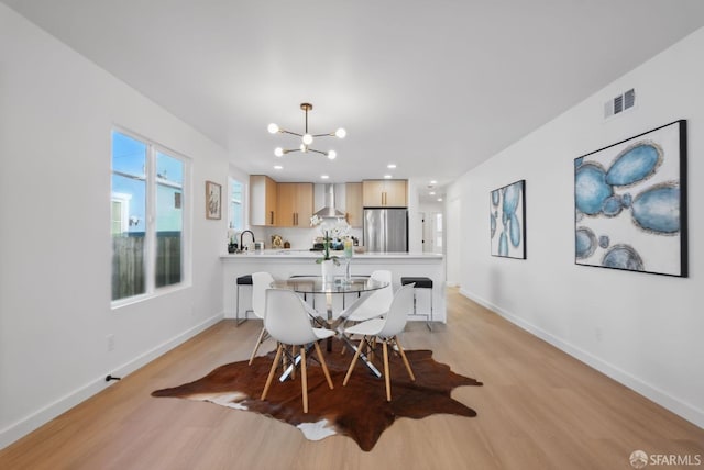 dining space featuring sink, light wood-type flooring, and a notable chandelier