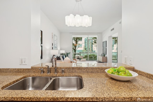 kitchen featuring visible vents, a sink, decorative light fixtures, light stone counters, and open floor plan