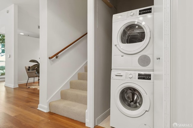 laundry room with laundry area, stacked washer and dryer, wood finished floors, and baseboards