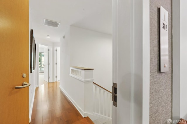 corridor with visible vents, an upstairs landing, baseboards, and wood finished floors