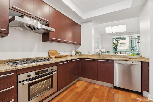 kitchen featuring light stone countertops, a sink, under cabinet range hood, appliances with stainless steel finishes, and light wood-type flooring