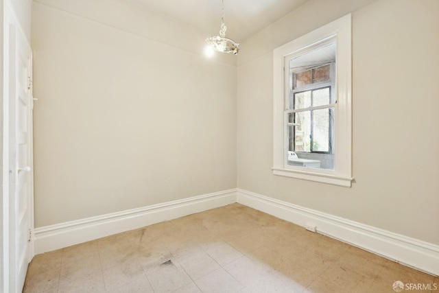spare room featuring a chandelier and baseboards