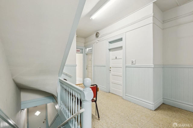 corridor featuring an upstairs landing, tile patterned floors, and wainscoting