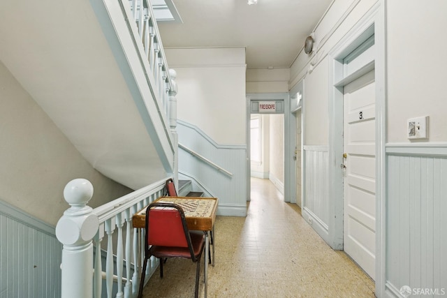 hallway with light floors, wainscoting, and an upstairs landing