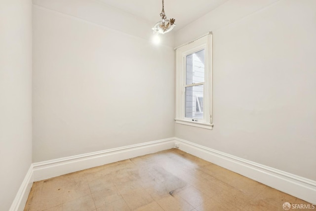 unfurnished room featuring baseboards and a chandelier
