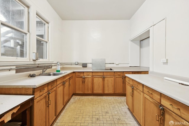 kitchen with a sink, light countertops, brown cabinets, and brick patterned floors