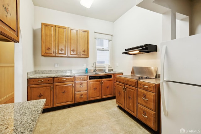 kitchen with freestanding refrigerator, a sink, under cabinet range hood, brown cabinetry, and light stone countertops