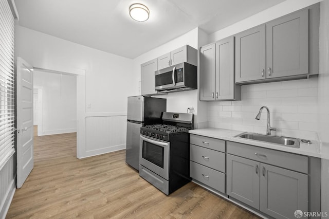 kitchen with gray cabinetry, sink, appliances with stainless steel finishes, and light hardwood / wood-style flooring