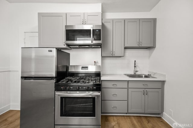 kitchen with dark hardwood / wood-style flooring, backsplash, gray cabinetry, stainless steel appliances, and sink