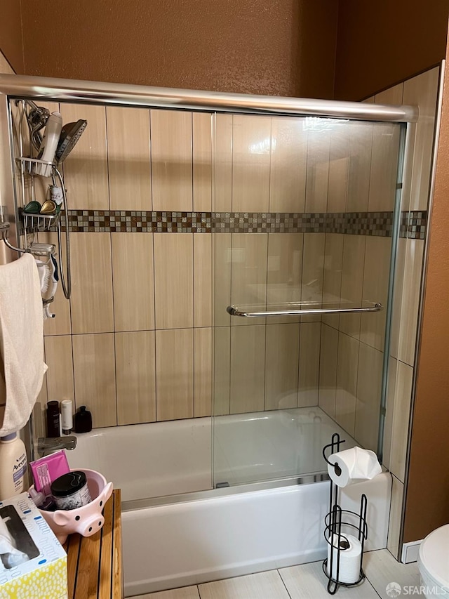 bathroom featuring enclosed tub / shower combo, tile patterned flooring, and toilet