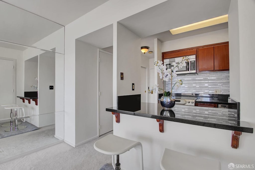 kitchen featuring light colored carpet, decorative backsplash, a kitchen bar, and kitchen peninsula