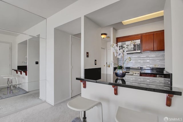 kitchen featuring light colored carpet, decorative backsplash, a kitchen bar, and kitchen peninsula