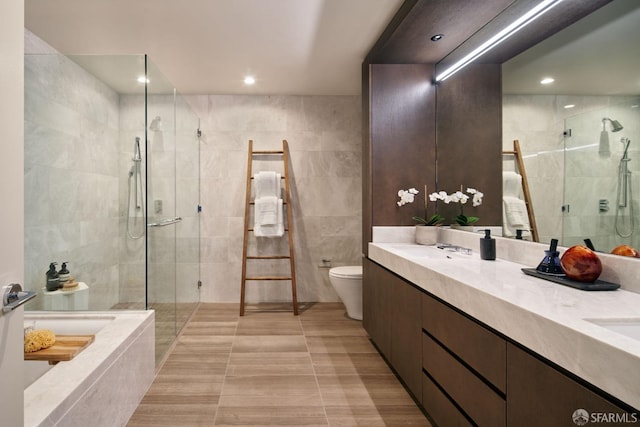 full bathroom featuring vanity, tile walls, shower with separate bathtub, and toilet