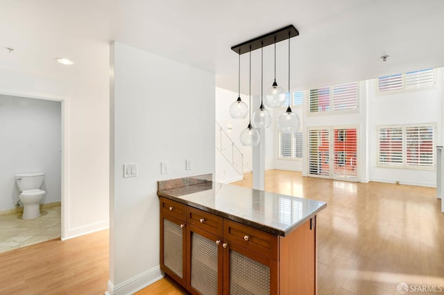 kitchen featuring kitchen peninsula, decorative light fixtures, light hardwood / wood-style flooring, and dark stone counters