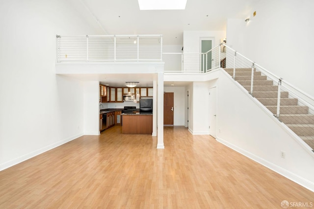 unfurnished living room with a high ceiling, sink, a skylight, and hardwood / wood-style floors