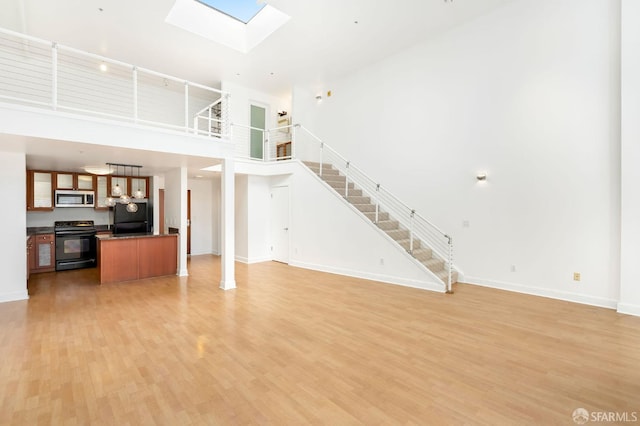 living room featuring a high ceiling, a skylight, and light hardwood / wood-style flooring