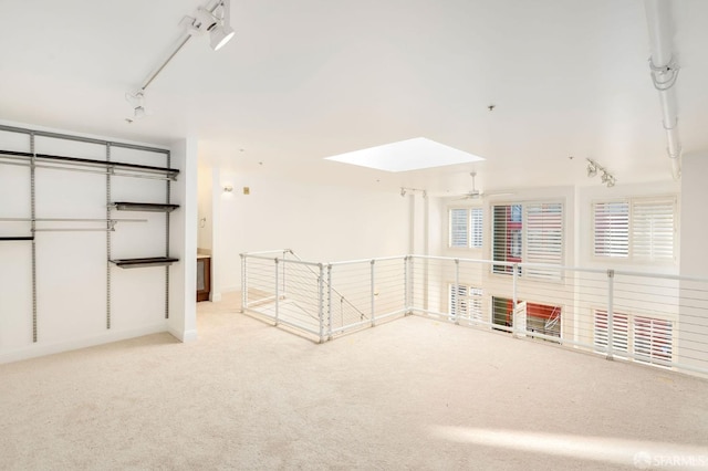 spare room with ceiling fan, light colored carpet, track lighting, and a skylight