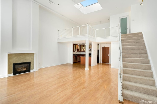 unfurnished living room with a skylight, hardwood / wood-style floors, a high ceiling, and sink