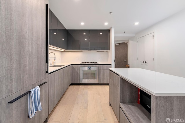 kitchen featuring oven, gray cabinets, a sink, modern cabinets, and light wood-style flooring