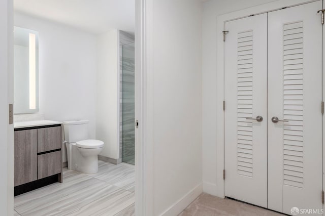 bathroom with toilet, a shower with door, vanity, and baseboards