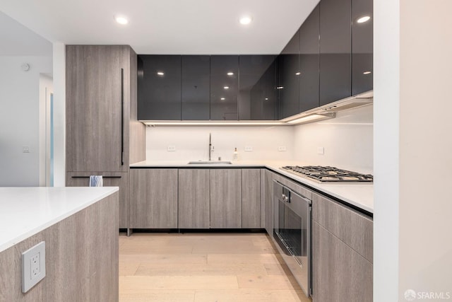 kitchen featuring light wood finished floors, wall oven, a sink, stainless steel gas stovetop, and modern cabinets
