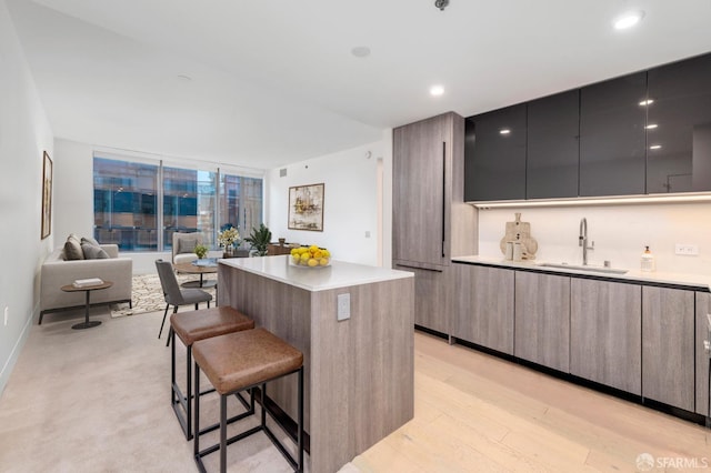 kitchen featuring a kitchen breakfast bar, a sink, modern cabinets, light countertops, and a kitchen island