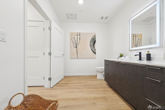 bathroom featuring toilet, vanity, wood finished floors, baseboards, and visible vents