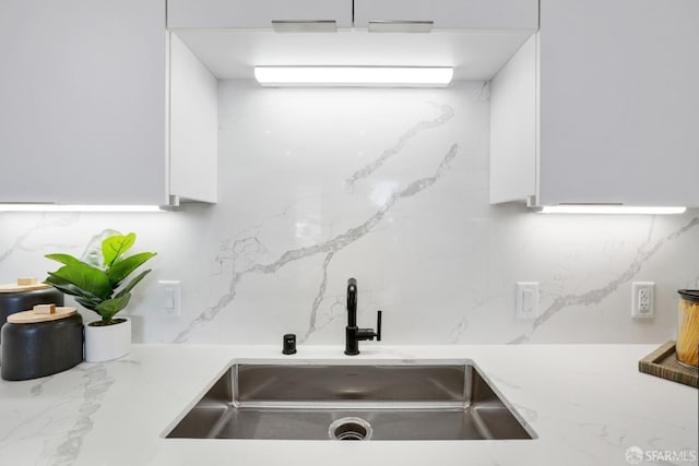kitchen with decorative backsplash, white cabinets, a sink, and light stone countertops