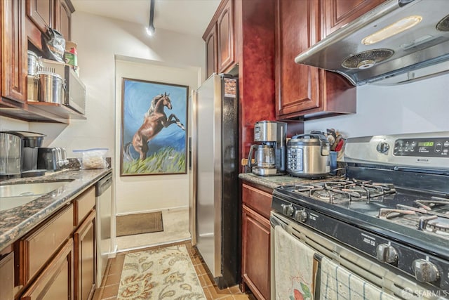 kitchen featuring sink, rail lighting, dark stone countertops, light tile patterned flooring, and appliances with stainless steel finishes